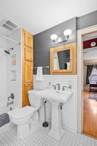 This stylish full bathroom features a classic pedestal sink, sleek subway tile shower, modern lighting, and natural wood accents for a warm, contemporary feel.