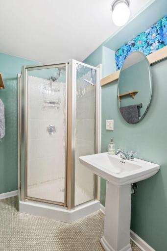 The lower-level 3/4 bathroom includes a sleek pedestal sink, a corner glass shower, and heated floorsâperfect as a lower-level suite.