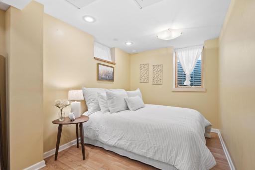 Comfort meets style in this basement third bedroom, featuring soft lighting, egress windows, and a clean, neutral design that makes the space feel bright and restfulâperfect for use as part of a private primary suite.