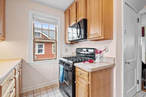 Cook with ease in this cozy and efficient kitchen space, featuring a gas stove, built-in microwave, and ample cabinet storage, all bathed in natural light from a charming window.