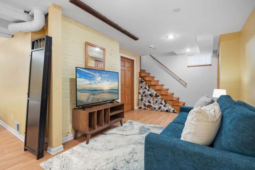 This cozy lower-level family room features wood-style flooring, exposed brick details, and custom stair accentsâperfect for movie nights or casual lounging.