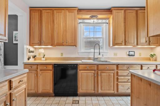 This well-appointed kitchen combines functionality and style with generous cabinet storage, under-cabinet lighting, a modern black dishwasher, and neutral tile flooring.