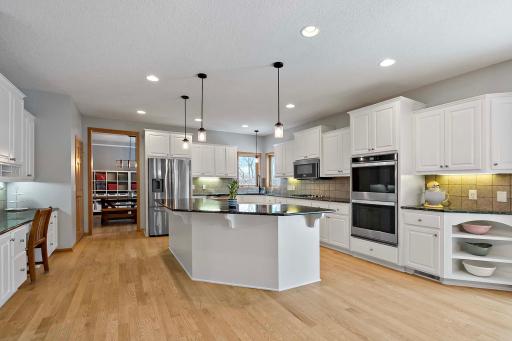Huge center island, built in desk, double ovens, gas cooktop, stone backsplash, hard surface countertops, and gorgeous hardwood floors throughout.