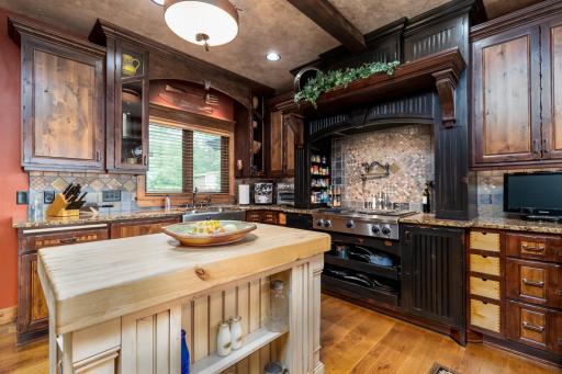 Chef’s kitchen with custom cabinetry, rich wood finishes, center island, and artistic stone backsplash.