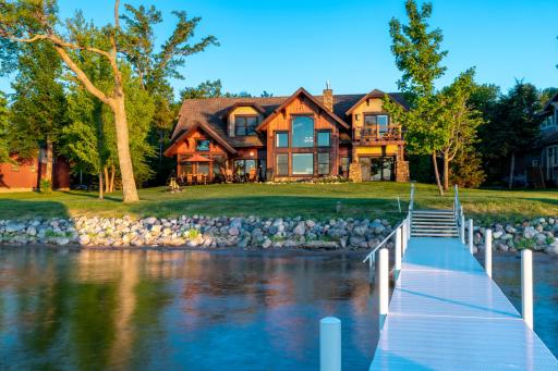 Lakeside view of home with manicured shoreline, stonework, and expansive windows.