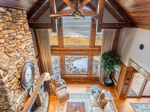 Soaring great room with vaulted ceilings, a full-height stone fireplace, and floor-to-ceiling lakeview windows.