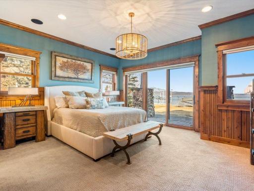 Lake-facing primary bedroom with tray ceiling, chandelier, and sliding glass door to private deck.
