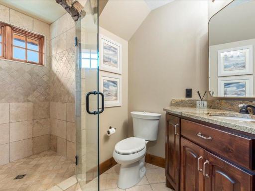 Stylish guest bathroom with walk-in glass shower, granite vanity, and natural tile.