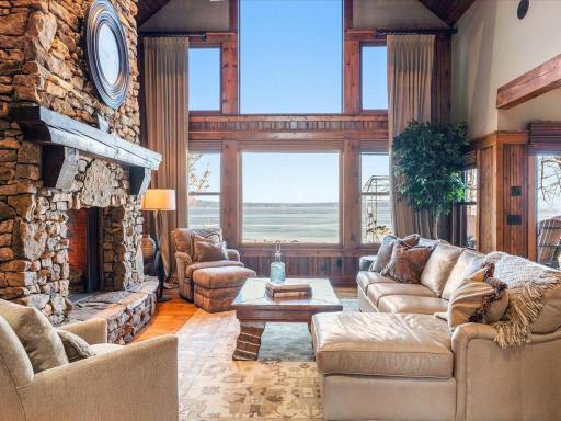 Sun-drenched great room with panoramic lake views, custom stone fireplace, and soaring wood-framed windows.