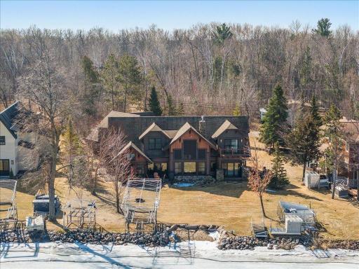 Drone view showcasing rear of the home, patio, and wooded privacy.