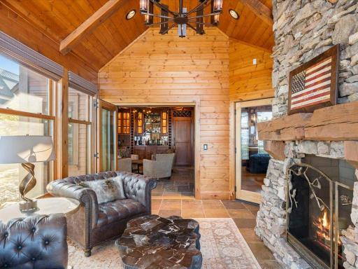 Lakeside sitting room with wood-paneled ceiling, stone fireplace, and seamless flow to the great room.
