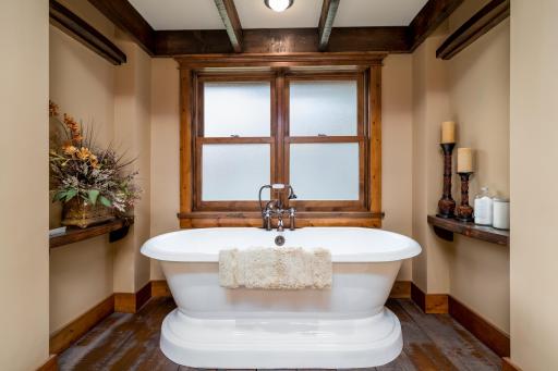 Luxurious ensuite with freestanding soaking tub, wood beam detail, and custom sconce lighting.
