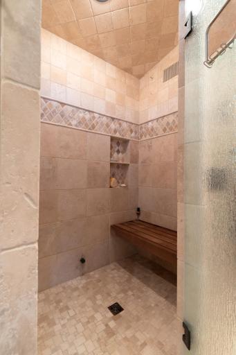 Custom walk-in shower with stone tile surround, built-in bench, and rain showerhead.