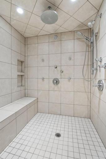 The walk in shower in the perfect place to relax after a long day with multiple shower heads and a bench.