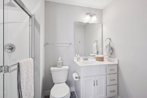 The en-suite bath features vanity sink with mirror, LVP flooring, wall lights and a step-in shower for convenience.