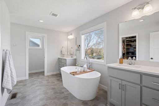 The primary bathroom boasts double vanities with sinks, a separate tub positioned under a picture window, and a separate shower.