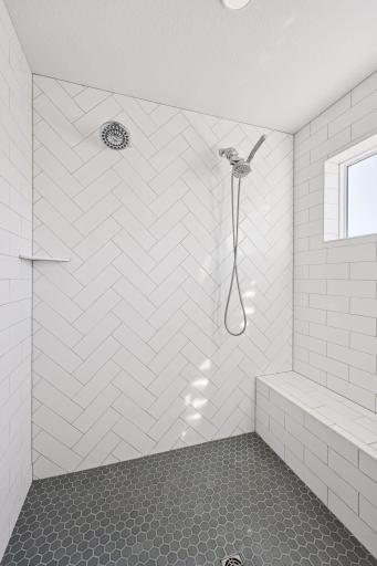 The spacious shower features elegant tile flooring and walls, along with a convenient built in bench.