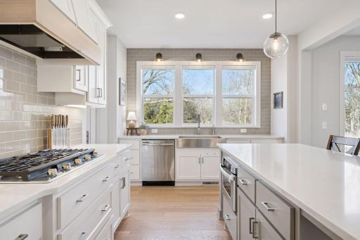 A large sink is perfectly positioned beneath three windows, offering beautiful views, while the tile backsplash and wall mounted lighting.