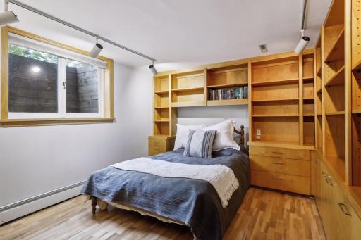 A bedroom with double egress windows is ideal for guests, with track lighting, walls of built-ins and hardwood flooring.