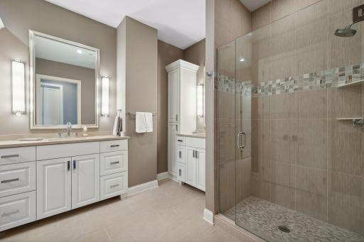 Primary bathroom with dual sinks, large walk-in shower and cabinet space for personal items