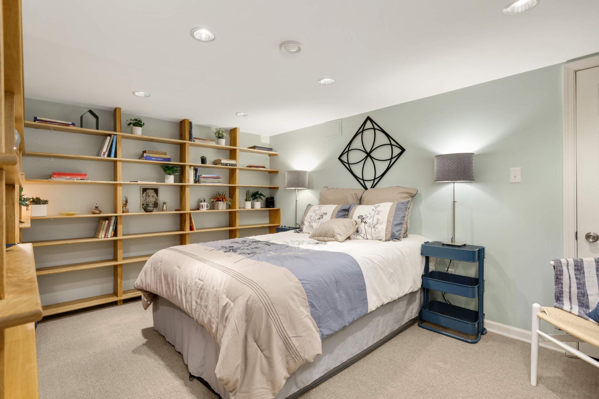 Cozy lower level guest room with ample space, open shelving, and a built-in Murphy desk, making it a versatile and functional space for visitors or a private retreat.