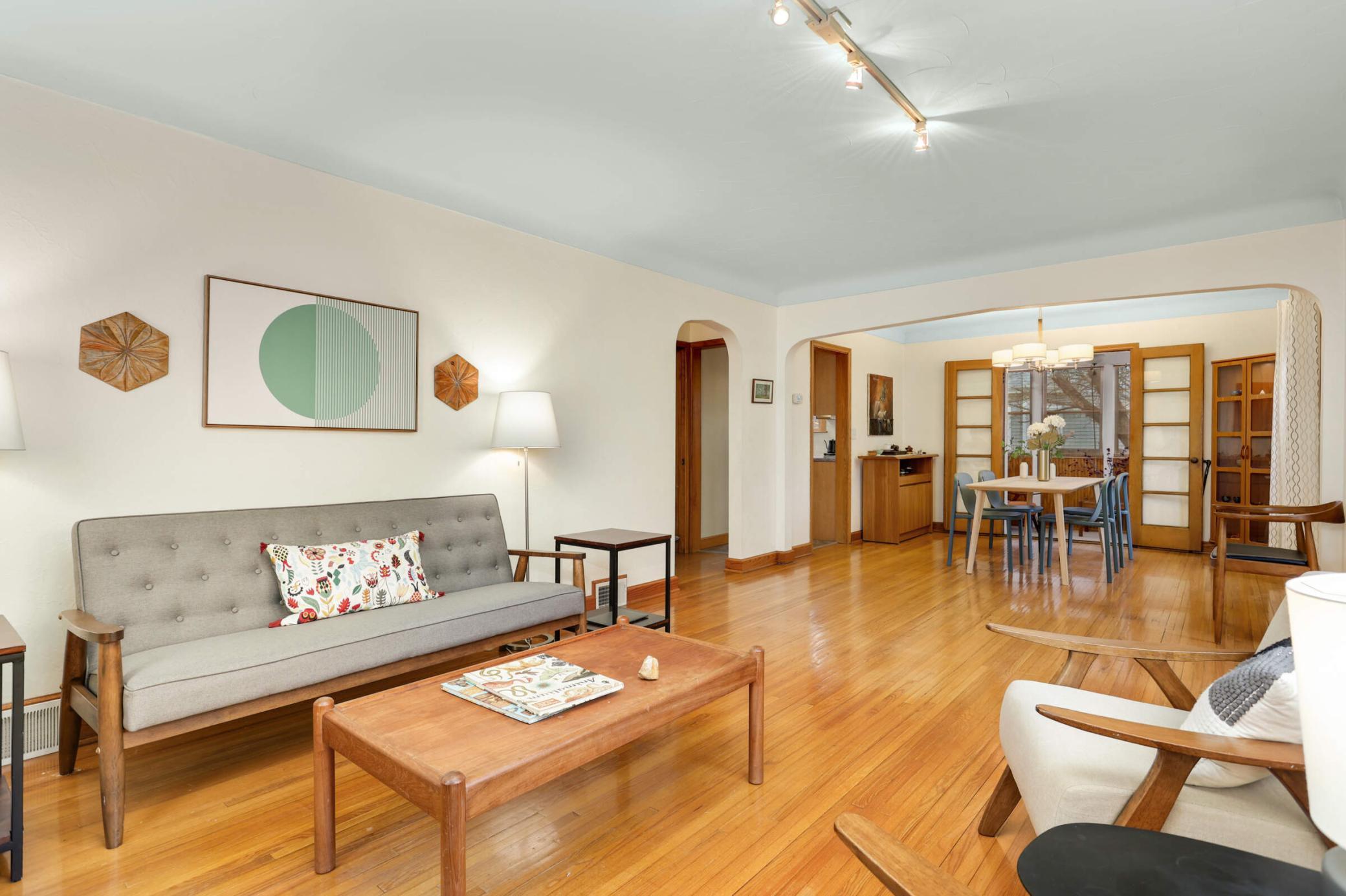 Inviting and spacious living room featuring warm hardwood floors and seamless flow into the dining and sunroom areas—perfect for relaxing or entertaining.
