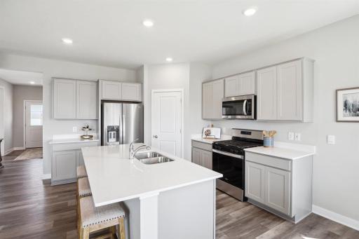 A spacious kitchen with a gas range, quartz countertops, and stainless appliances. *Photos of former model home, selections shown will vary.