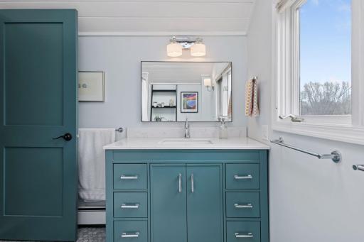 Upper level full bath. Cute vanity sink, wall light, tile floors, vaulted ceiling and skylight.