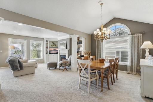 The vaulted formal dining room features an arched window and opens seamlessly into the living room, creating a spacious and connected feel with windows on all sides bringing in abundant natural light.