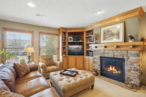A beautiful stone-surround gas fireplace anchors this lower-level space, framed by rich wood built-ins, detailed crown molding, and large lookout windows that fill the room with natural light.