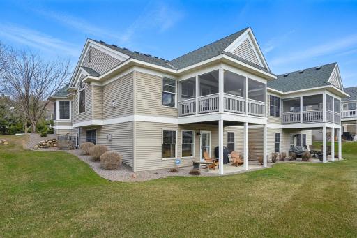 A view of the homeâs back exterior shows the walkout lower level, covered patio, and vaulted screened porchâall overlooking the well-maintained yard and surrounding greenspace.
