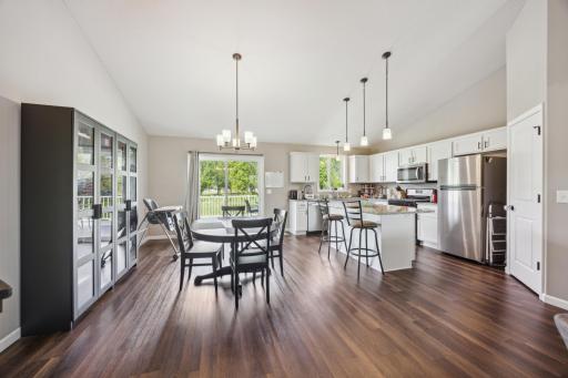 A spacious dining area seamlessly connected to a bright kitchen, featuring elegant light fixtures, wood flooring, and sliding doors that offer natural light and backyard views