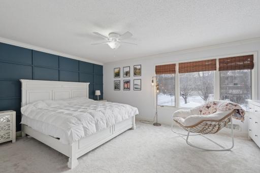 Spacious primary bedroom showcasing a designer accent wall, ceiling fan, and carpeted flooring. Abundant windows provide excellent natural light and peaceful views.