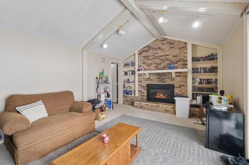 Cozy yet open lower-level living room featuring a brick fireplace, built-in shelving, and track lighting. The end-unit layout provides additional daylight and a comfortable, airy feel.