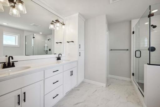 Owner's bathroom with double vanities and large linen cabinet. Photos, virtual/video tours may not depict actual home. Features, materials & finishes shown may contain options that are not included in price.