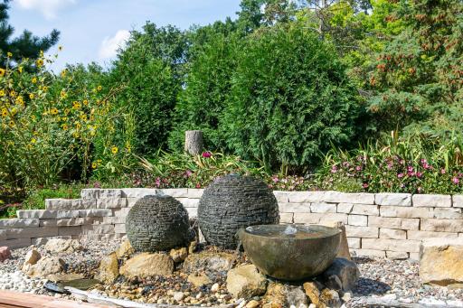 What a stunning tranquil outdoor scene featuring three bubbling fountains as the central focal point of the backyard. Water gently bubbles & flows down their rounded surfaces, creating a soothing sound and visual effect. VERY EZ to maintain as well