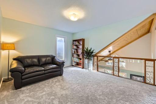 This loft is designed as a relaxed and functional living space, perhaps a reading nook, a small living room, or a quiet retreat. The open design connects it to the rest of the home & the glass panel railing allows light to flow through