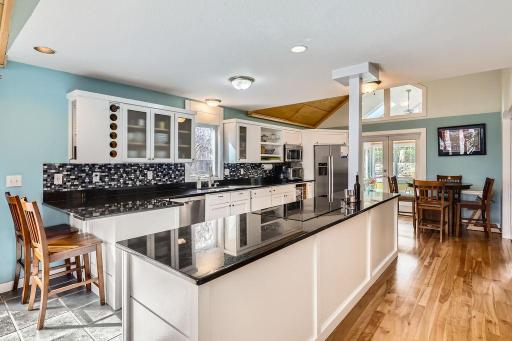 This dream kitchen features newer stainless appliances, a gorgeous tile backsplash, tile flooring in the kitchen area transitioning into warm wood flooring flowing from the living room into the dining area.
