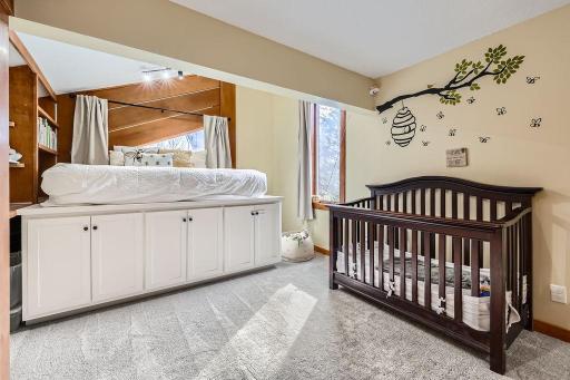 A raised sleeping platform dominates the left side of the room. This platform is built on top of a set of white cabinets with simple black knobs, providing ample storage underneath. This design still leaves plenty of space in this room