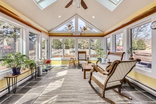 This is a bright and airy sunroom, designed to bring the outdoors in. The numerous large windows on all sides, including striking triangular windows that follow the pitch of the vaulted ceiling + skylights allow for an abundance of light year round