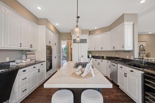 This chefâs kitchen is designed for both functionality and style with crisp white cabinetry, granite countertops, a large center island with stained cabinetry, and breakfast bar seating.