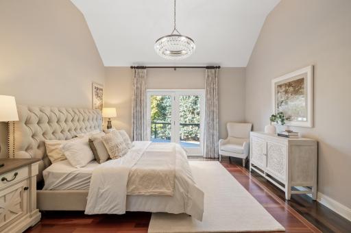 The main-level primary suite is an oasis of comfort, featuring private access to the deck through glass French doors, an updated chandelier, and custom hardwood floors.