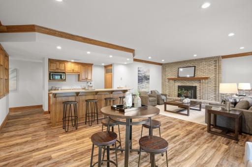 The expansive walk-out lower-level family room is perfect for entertaining, featuring newer luxury vinyl plank flooring, cozy brick accent walls, and a stylish wood-burning fireplace.