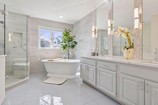 Elegantly updated primary bath features a large soaker tub, glass walk-in shower, dual vanities, beautiful fixtures and tile, plus great storage space