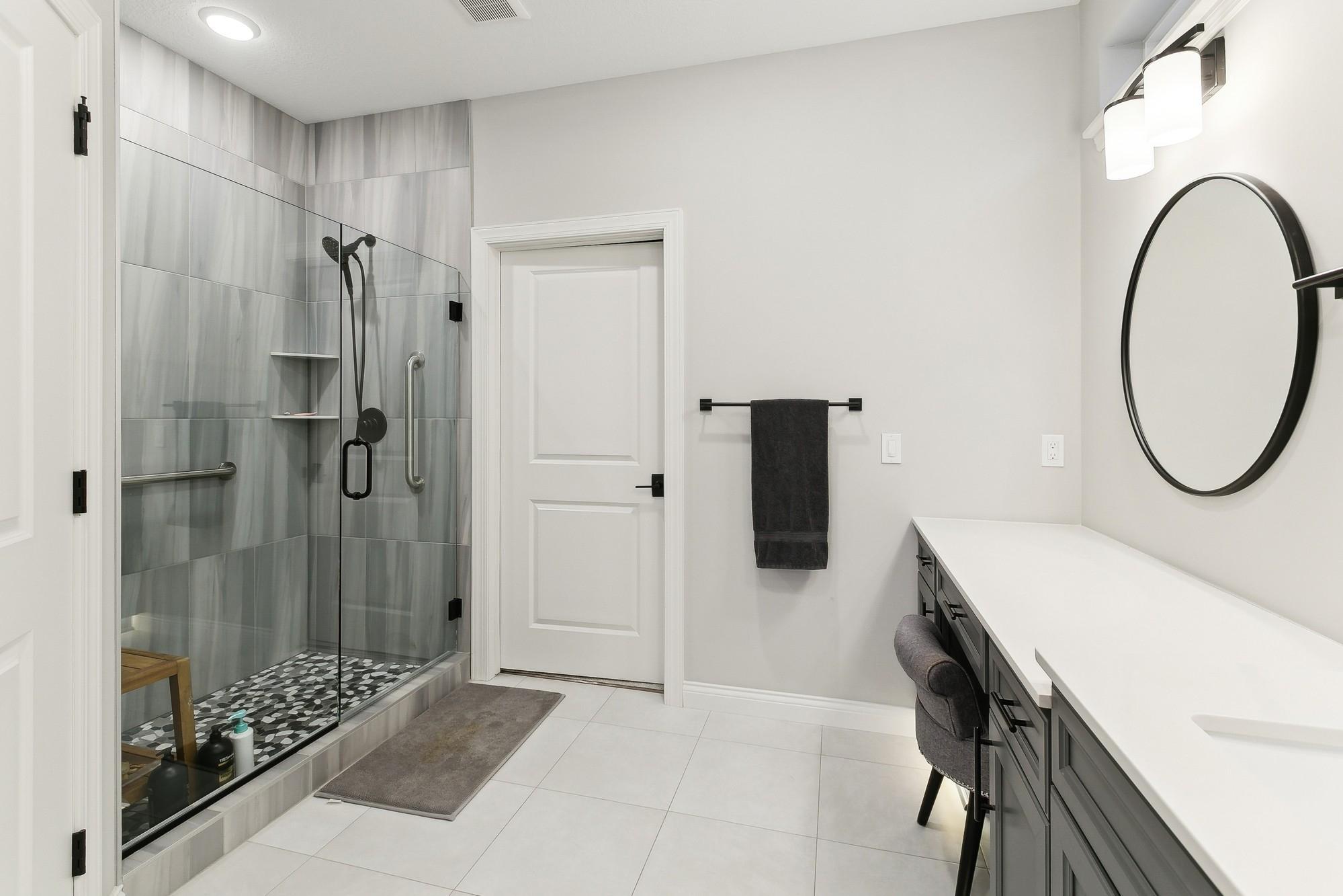 Large primary shower with tiling up to the ceiling, seamless glass doors and convenient grab bars.