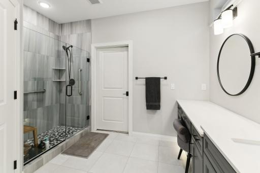 Large primary shower with tiling up to the ceiling, seamless glass doors and convenient grab bars.