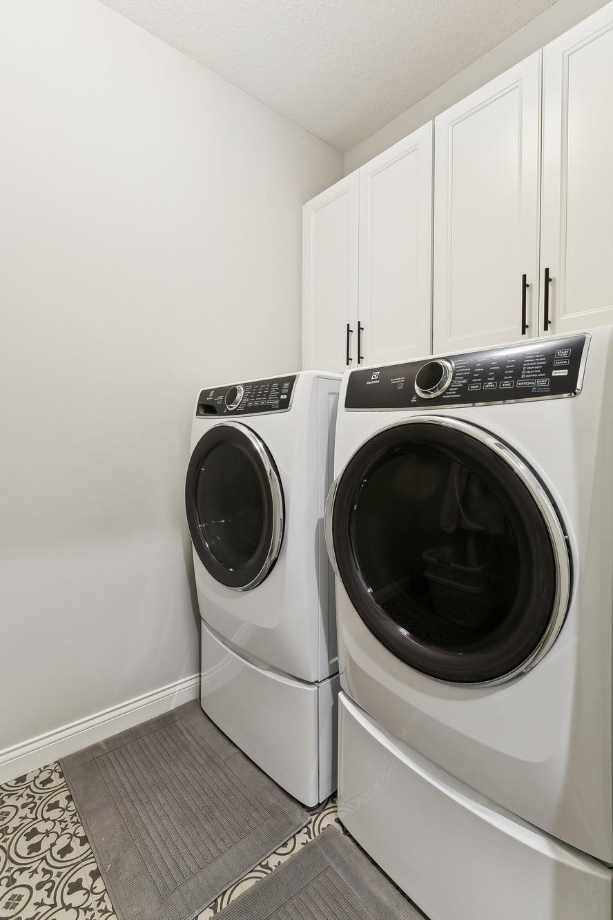 Laundry room with cabinet space and hanging for storage and organization. Washer and dryer are on pedestals for easier loading.