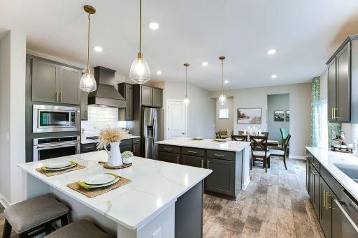 The gourmet kitchen features upgraded Kitchen Aid appliances with a 5-burner gas cooktop, stainless appliances, Wood hood vent, and an amazing dishwasher! *Photo of model home. Colors and selections shown are different.