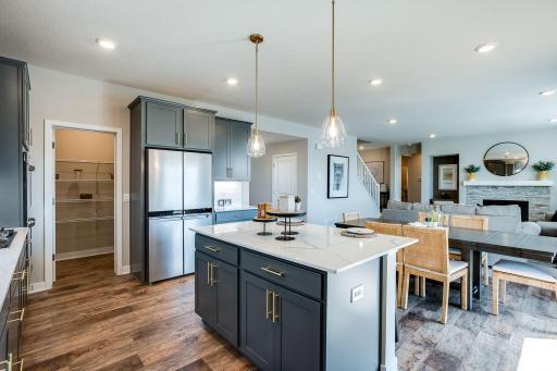 Dark gray cabinetry complimented beautifully by brass cabinet hardware and pendant lights, and hard surface flooring with a beautiful, warm tone.