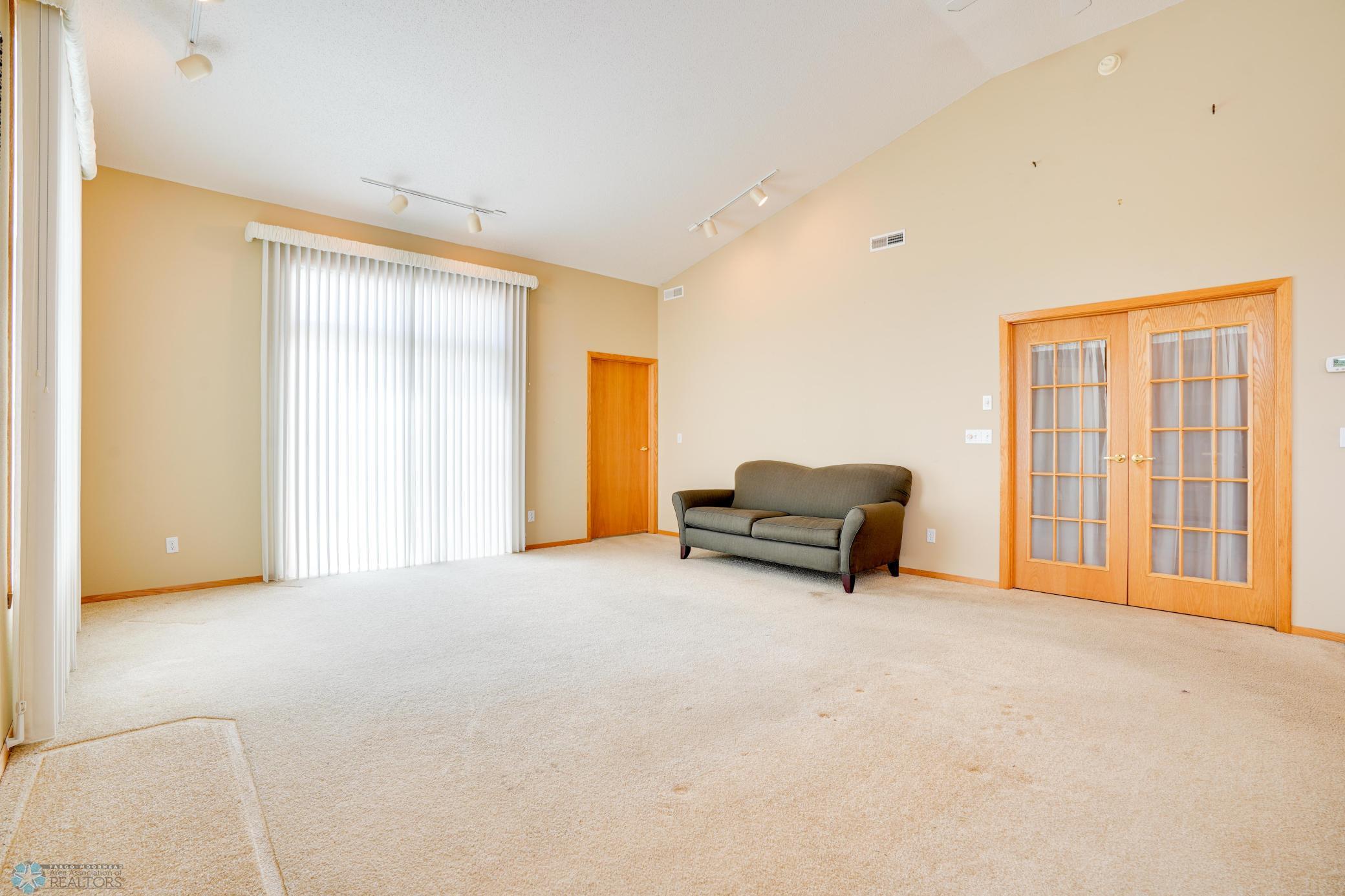 Spacious living room with vaulted ceiling, track lighting, walk-out to patio